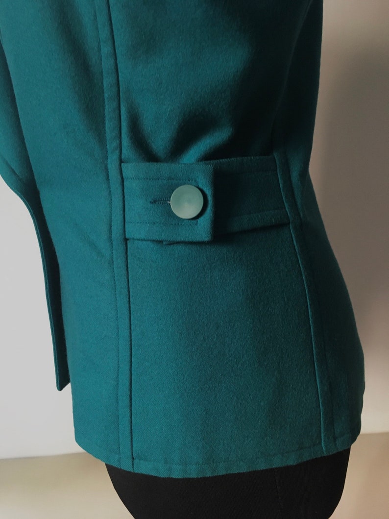 May include: A teal blue blazer with a single button on the back pocket.