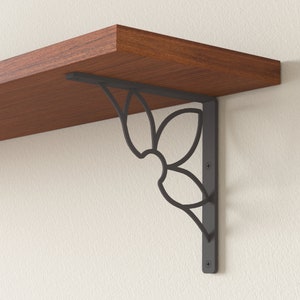 May include: Black metal shelf bracket with a decorative floral design. The bracket is attached to a wooden shelf.