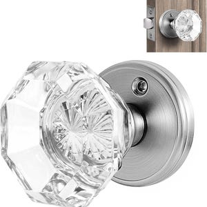 May include: A clear, faceted glass door knob with an octagonal shape, attached to a circular, brushed nickel metal rosette. The knob features a starburst pattern in the center and is shown mounted on a wooden door in the upper right corner.