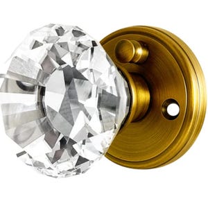 May include: A faceted crystal door knob with a brass-colored base and backplate. The knob is clear and reflects light, while the base has a vintage, antique finish. This decorative hardware adds a touch of elegance.
