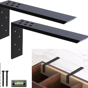May include: Two L-shaped black metal shelf brackets with pre-drilled mounting holes, accompanied by a drill bit, two screws, and a small spirit level. The brackets are shown installed on a wooden structure with a white tiled surface above.