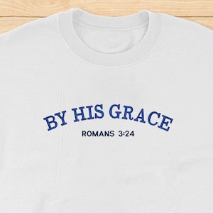 May include: White sweatshirt with blue text that reads "By His Grace Romans 3:24".