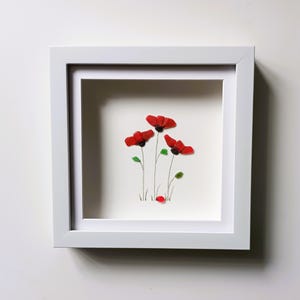 May include: Framed artwork featuring a cluster of red poppies made from sea glass, with green glass leaves and stems. The artwork is set against a white background.