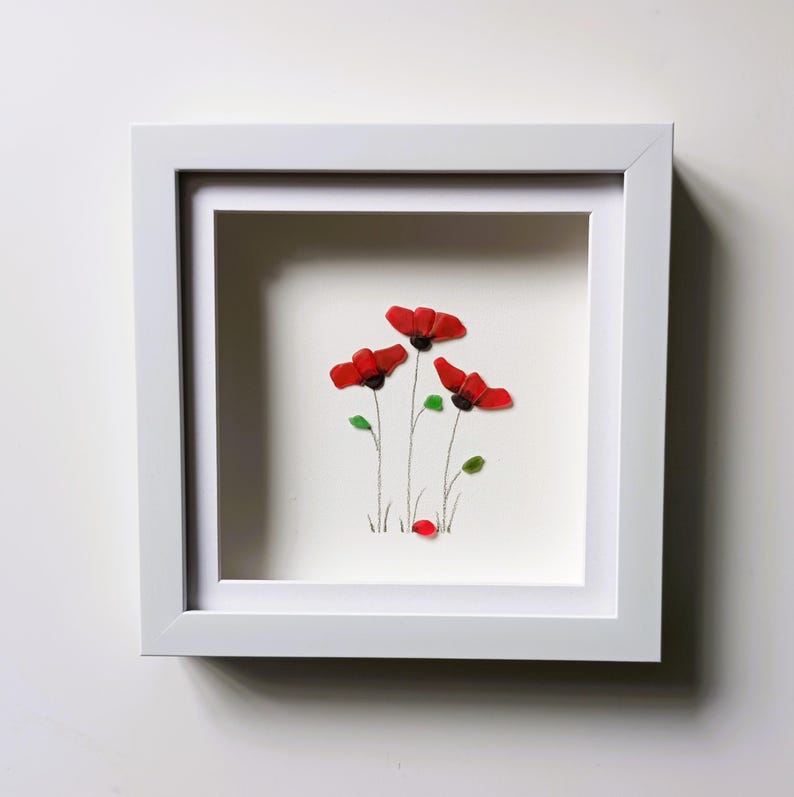 May include: Framed artwork featuring a cluster of red poppies made from sea glass, with green glass leaves and stems. The artwork is set against a white background.