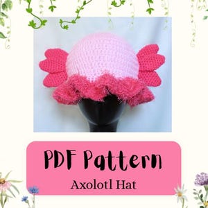 Puede incluir: Un gorro de ganchillo rosa claro con dos branquias laterales de color rosa brillante y un borde texturizado con volantes de color rosa oscuro. Debajo, un gráfico rectangular rosa muestra el texto negro PDF Pattern y Axolotl Hat.