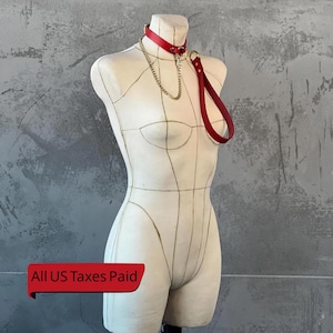 May include: A red leather collar with a matching leash and a gold-colored chain, displayed on a mannequin. The collar is secured with a buckle. The leash has a loop for the hand.