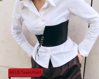 Puede incluir: Un corsé negro con cordones en la parte delantera y cierre de cremallera. El corsé se lleva sobre una camisa blanca abotonada. La imagen también incluye pantalones cortos marrones. El texto "All US Taxes Paid" está en una pancarta roja.