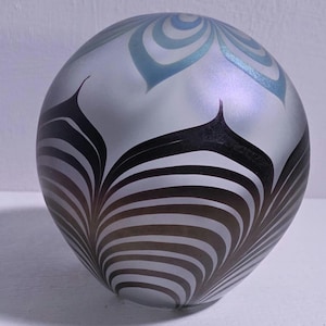 May include: A decorative glass sphere with a frosted finish. The sphere features a pattern of black and brown curved lines, with accents of light blue and white swirls at the top. The design is symmetrical and elegant.