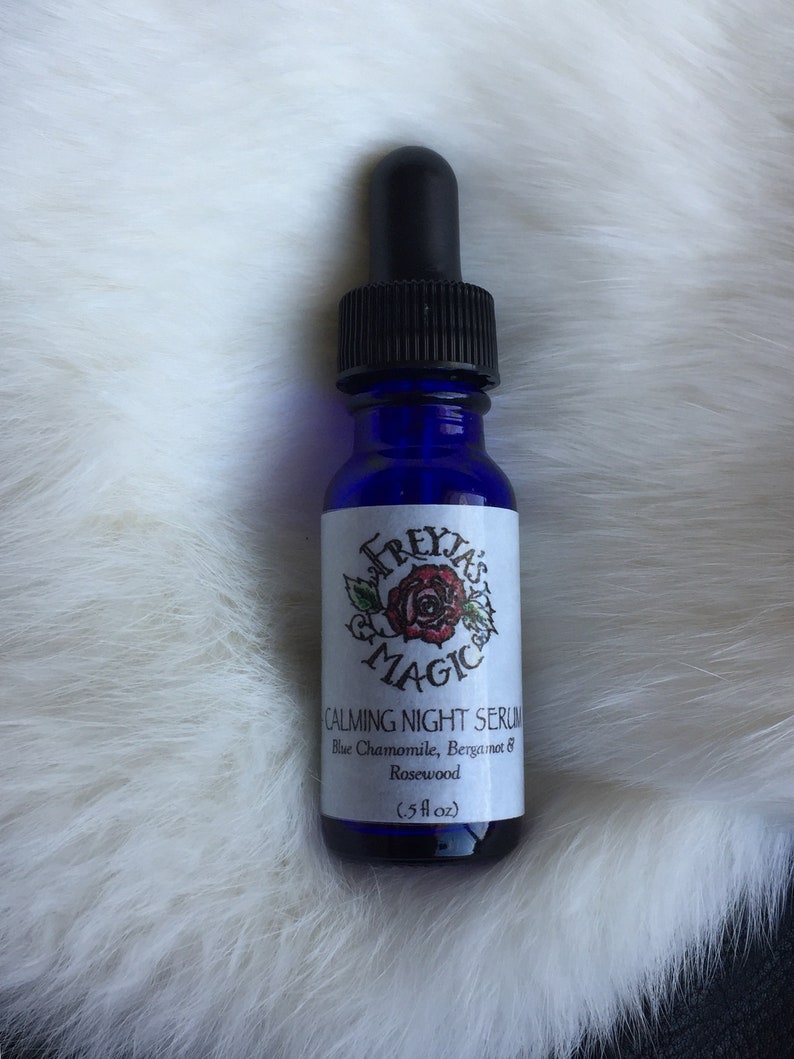 May include: A blue glass bottle with a black dropper top. The bottle is labelled "Freyja's Magic Calming Night Serum Blue Chamomile, Bergamot & Rosewood (.5 fl oz)"