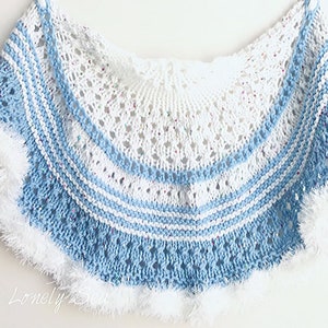May include: A handmade, knitted shawl in a half-circle shape. The shawl features a white and light blue color scheme with a textured pattern. The edges are trimmed with white, fluffy yarn. The Lonely Sea is written in the bottom left corner.