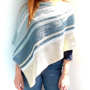 Könnte beinhalten: Ein gestrickter Poncho mit einem Farbverlauf in Blau-, Petrol- und Cremetönen. Das Kleidungsstück weist ein strukturiertes Strickmuster mit horizontalen Streifen und einen asymmetrischen Saum auf, der über Schultern und Oberkörper fällt.