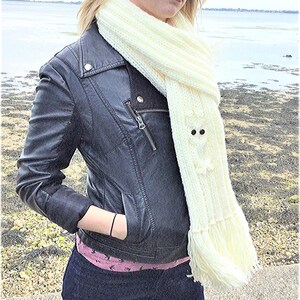 May include: A white knitted scarf with a fringe. The scarf has a knitted owl design with black button eyes.