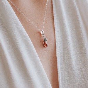 Op de afbeelding: Een zilveren ketting met een kleine hanger van barnsteen. De hanger is gezet in een zilveren frame met een delicaat bloemenmotief.