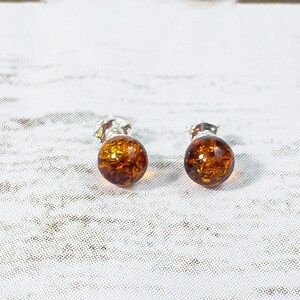 May include: A pair of amber stud earrings with silver settings. The earrings are round and have a translucent amber color.