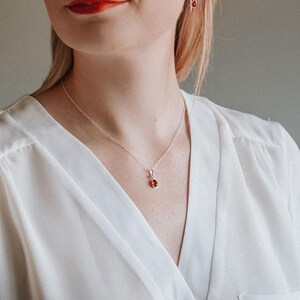 Puede incluir: Un collar de cadena de plata con un peque&ntilde;o colgante en forma de l&aacute;grima con una piedra roja.