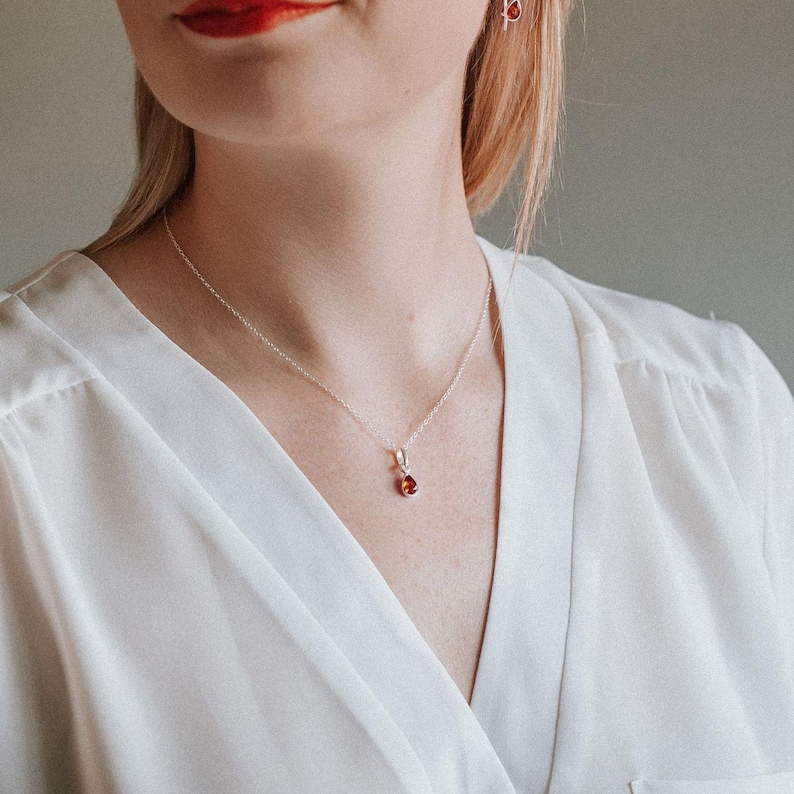 Puede incluir: Un collar de cadena de plata con un peque&ntilde;o colgante en forma de l&aacute;grima con una piedra roja.