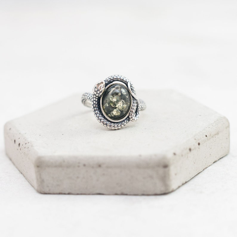Peut inclure: Une bague en argent avec une pierre pr&eacute;cieuse verte sertie dans un motif de serpent.