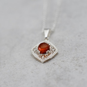May include: A silver pendant necklace with a red gemstone set in a filigree design.