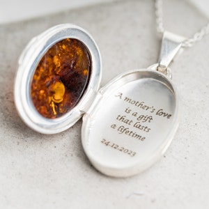 Op de afbeelding: Zilveren ketting met een hanger met een amberkleurige steen erin. De hanger is open en aan de binnenkant staat de tekst "A mother's love is a gift that lasts a lifetime 24.12.2023" gegraveerd.