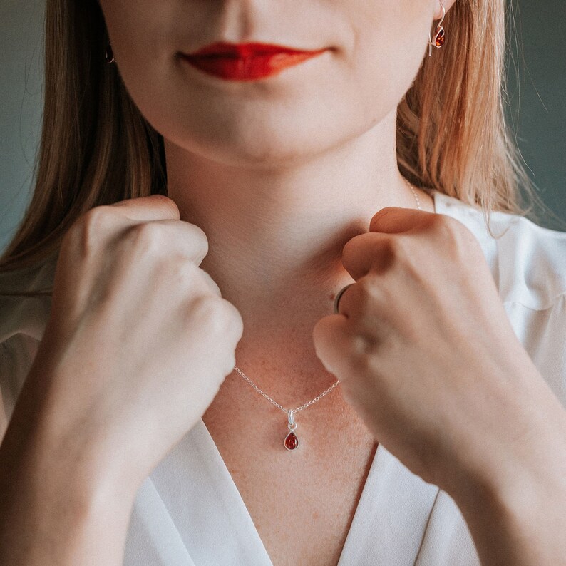 Puede incluir: Un collar de plata con un colgante de piedra roja en forma de l&aacute;grima.