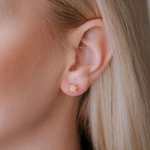 Peut inclure: Gros plan sur l'oreille d'une personne avec une petite boucle d'oreille ronde en pierre précieuse jaune.