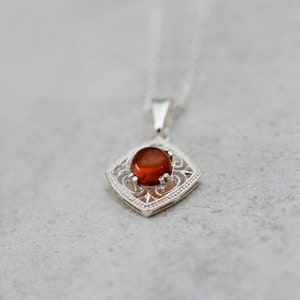 May include: A silver pendant necklace with a red gemstone set in a filigree design.