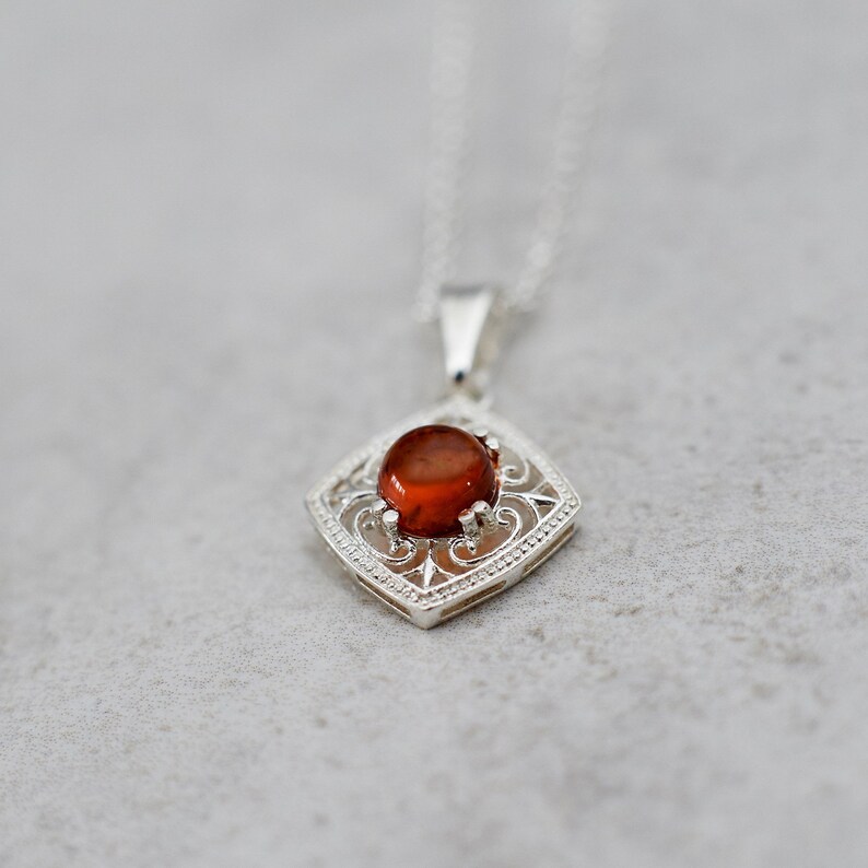 May include: A silver pendant necklace with a red gemstone set in a filigree design.