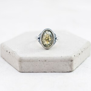 May include: A silver ring with an oval-shaped green amber stone set in a detailed silver bezel.
