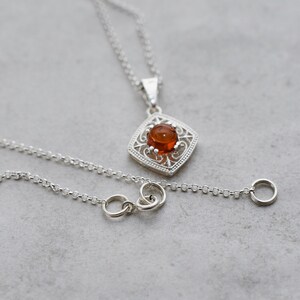 May include: A silver chain necklace with a pendant featuring a round amber stone set in a filigree design.
