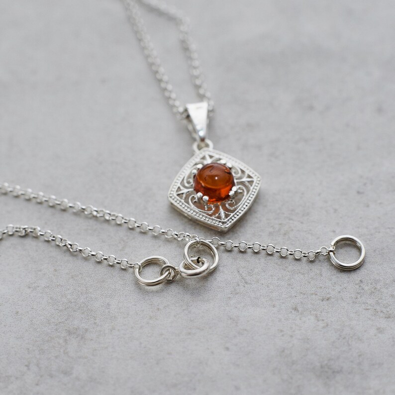 May include: A silver chain necklace with a pendant featuring a round amber stone set in a filigree design.