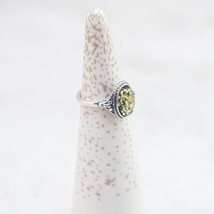 May include: A silver ring with an oval-shaped green amber stone set in a decorative filigree design.