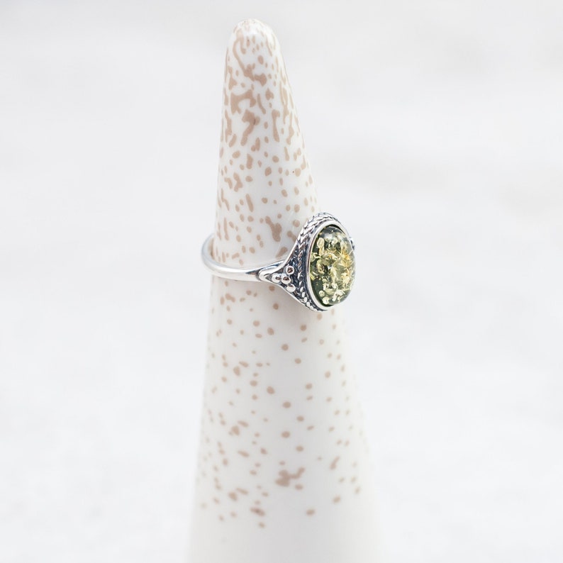 May include: A silver ring with an oval-shaped green amber stone set in a decorative filigree design.