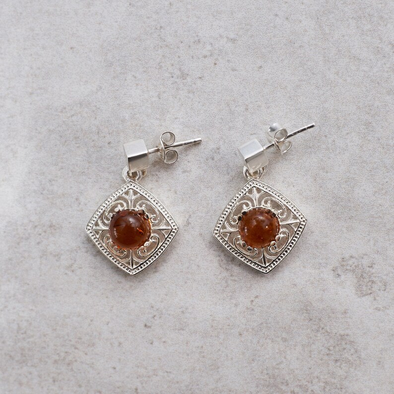 May include: A pair of silver earrings with a square-shaped design and a brown gemstone in the center.