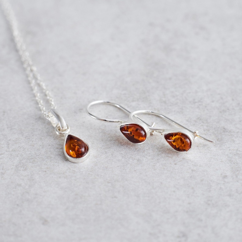 Puede incluir: Un conjunto de pendientes de gota de &aacute;mbar y un collar a juego. Los pendientes son de plata con una piedra de &aacute;mbar en forma de gota. El collar es una cadena de plata con un colgante de &aacute;mbar en forma de gota.