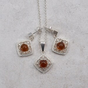 May include: A silver necklace and earrings set with a brown gemstone in a square filigree design.