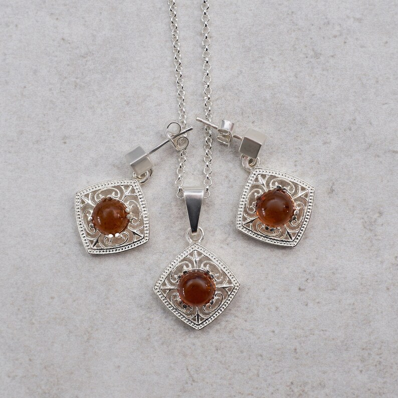 May include: A silver necklace and earrings set with a brown gemstone in a square filigree design.