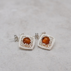 May include: A pair of silver earrings with amber stones set in a filigree design.