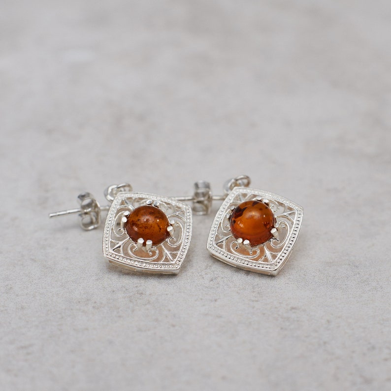 May include: A pair of silver earrings with amber stones set in a filigree design.