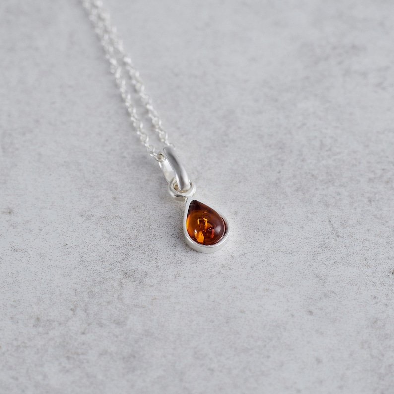 Puede incluir: Un collar de cadena de plata con un colgante en forma de l&aacute;grima con una piedra de &aacute;mbar marr&oacute;n.