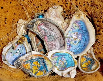 May include: A collection of oyster shell ornaments with maps of various locations printed on the inside. The shells are decorated with gold paint and have a rustic, coastal feel.