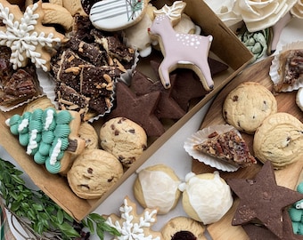 Könnte beinhalten: Eine Auswahl an dekorierten Keksen in einer Pappschachtel und auf einem Holztablett. Die Kekse umfassen eine Schneeflocke, einen Weihnachtsstrumpf, ein Reh und Sternformen. Andere Kekse sind rund und mit Nüssen oder Zuckerguss belegt.