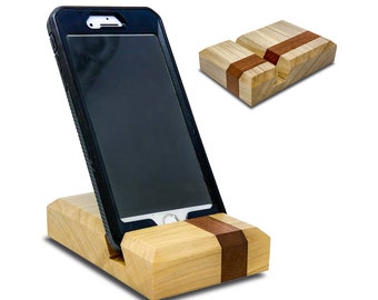 Op de afbeelding: Een houten telefoonstandaard met een natuurlijke houten afwerking en een donkerbruine accentstrook. De standaard is ontworpen om een smartphone rechtop te houden.