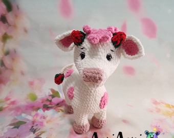 May include: A white crocheted cow with pink accents and red flowers. The cow has pink spots and a pink nose. The cow is standing on a floral background.