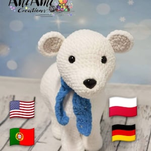 Op de afbeelding: Witte gehaakte ijsbeer met een blauwe sjaal. De beer staat op een wit houten oppervlak. De vlaggen van de Verenigde Staten, Polen, Duitsland en Portugal zijn zichtbaar op de achtergrond.
