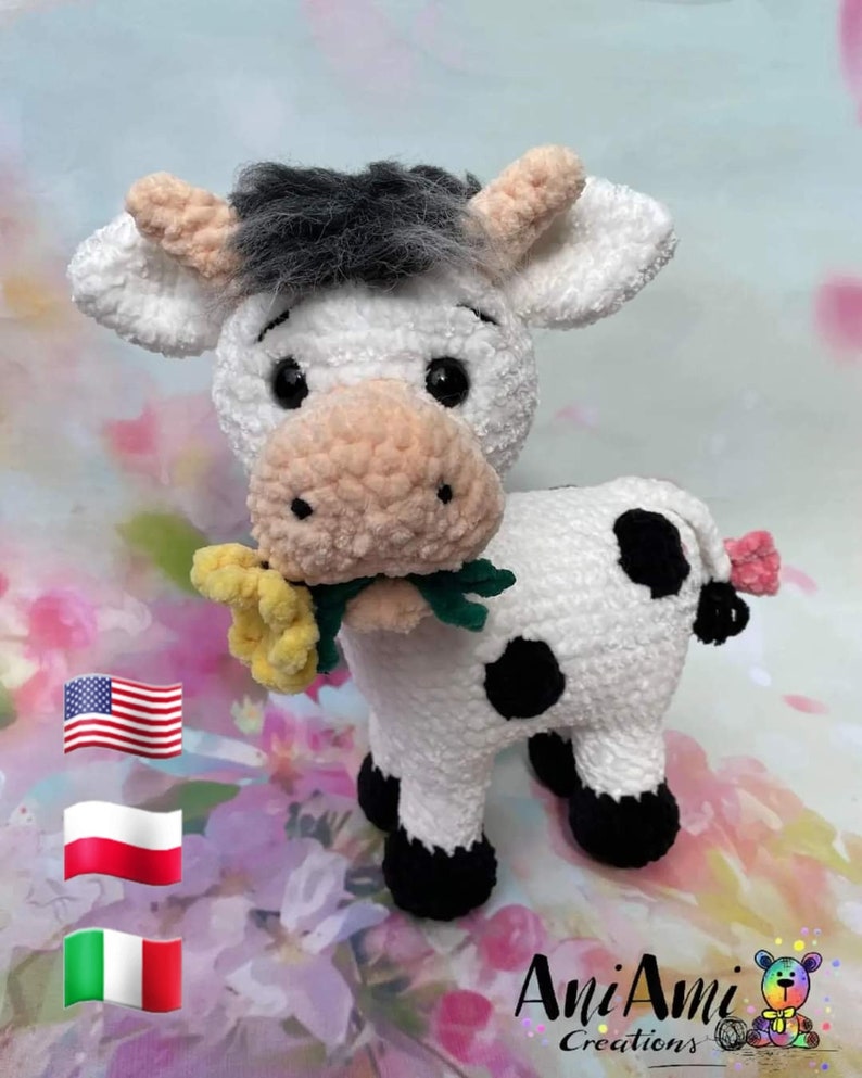 Puede incluir: Una vaca blanca de crochet con manchas negras que sostiene una flor amarilla en su boca. La vaca tiene pezu&ntilde;as negras y una cara blanca y negra. El fondo es un patr&oacute;n floral borroso.
