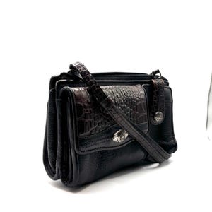 May include: A white ceramic mug with a black handle and the text "But First, Coffee" in a bold, black font. The mug is set against a blurred background, suggesting a cozy setting.