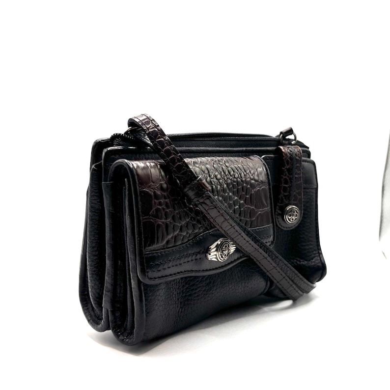 May include: A white ceramic mug with a black handle and the text "But First, Coffee" in a bold, black font. The mug is set against a blurred background, suggesting a cozy setting.