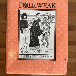 May include: A rectangular sewing pattern envelope in peach with a white border. The front features the text FOLKWEAR 134 and SOUTH ASIAN TOPS & WRAPS, with a black and white illustration of three figures wearing various traditional garments.