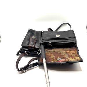 May include: Black leather crossbody bag with multiple compartments. Features a textured exterior, a decorative clasp, and a brown strap. The interior lining has a floral pattern. Includes a silver selfie stick.