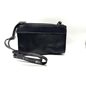 May include: Black leather crossbody bag with a long, adjustable strap. The bag has a rectangular shape with a zippered top and a textured surface. The strap features a brown and black pattern.